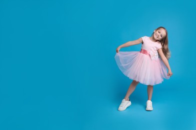 Photo of Cute little girl in beautiful dress dancing on light blue background. Space for text