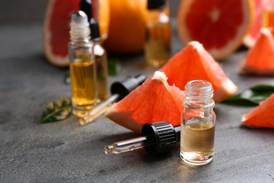 Bottles of essential oil and grapefruits on grey table, space for text