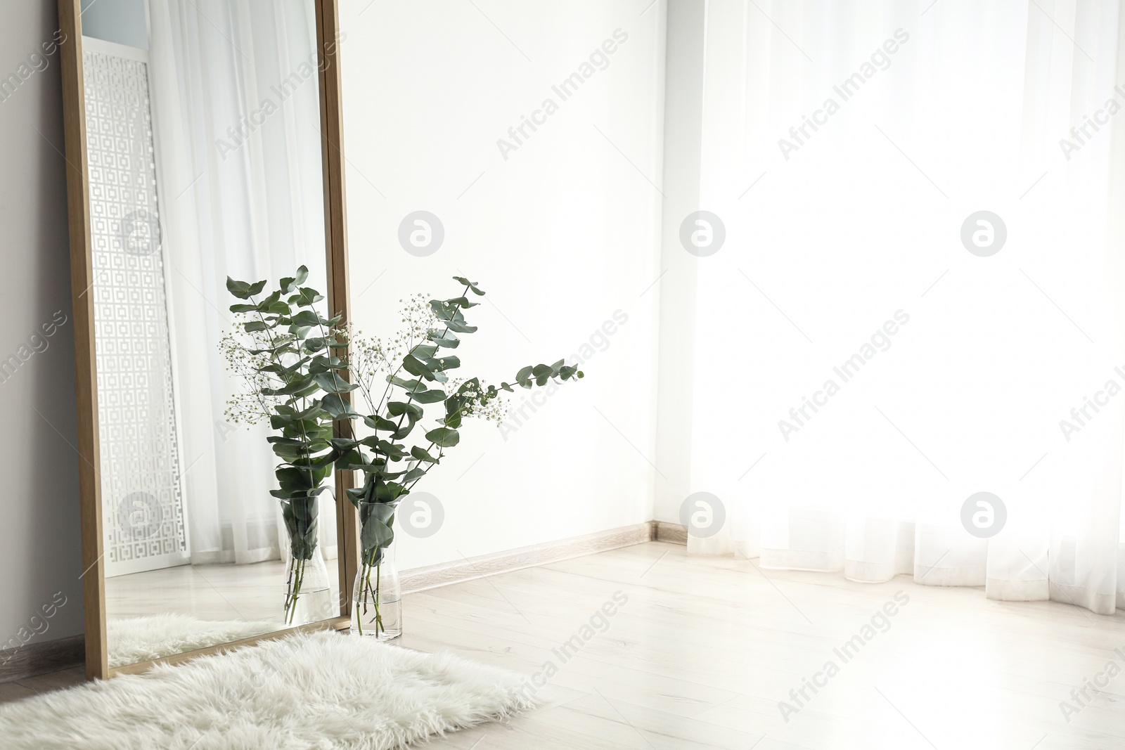 Photo of Large mirror with wooden frame near window in light room