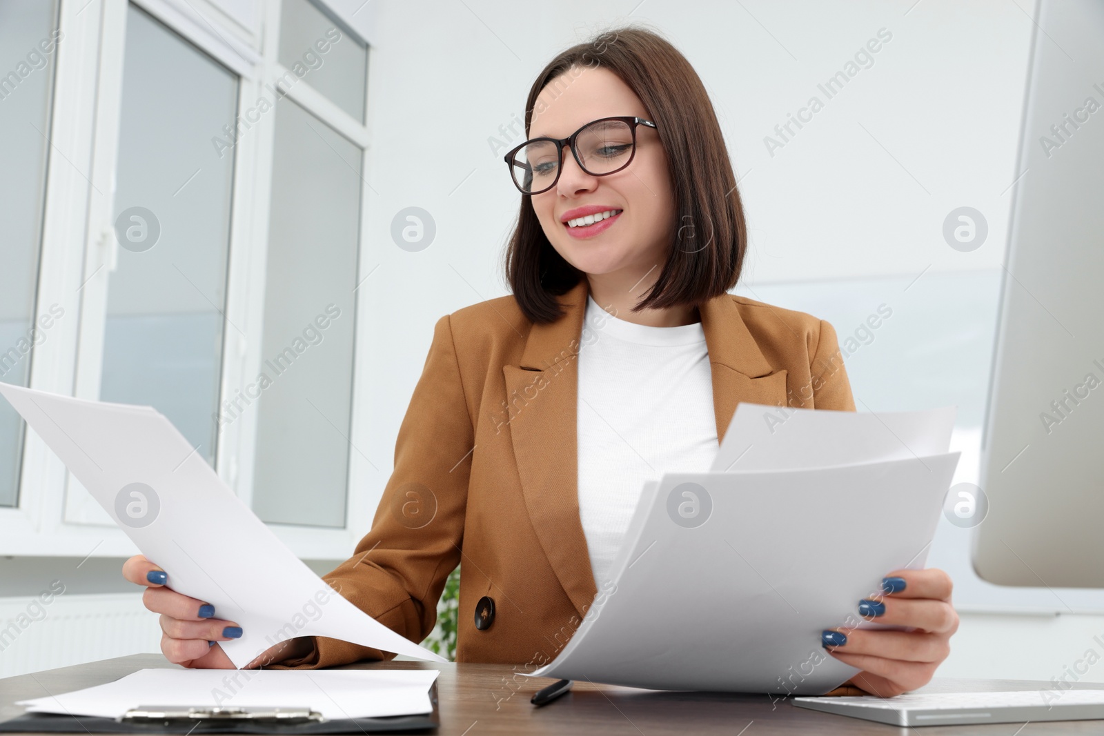Photo of Happy young intern working with paper sheets at table in modern office