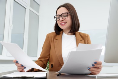 Photo of Happy young intern working with paper sheets at table in modern office