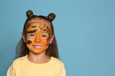 Cute little girl with face painting on blue background. Space for text