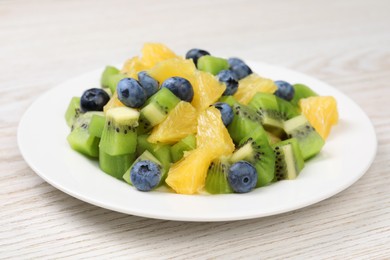 Plate of tasty fruit salad on white wooden table, closeup