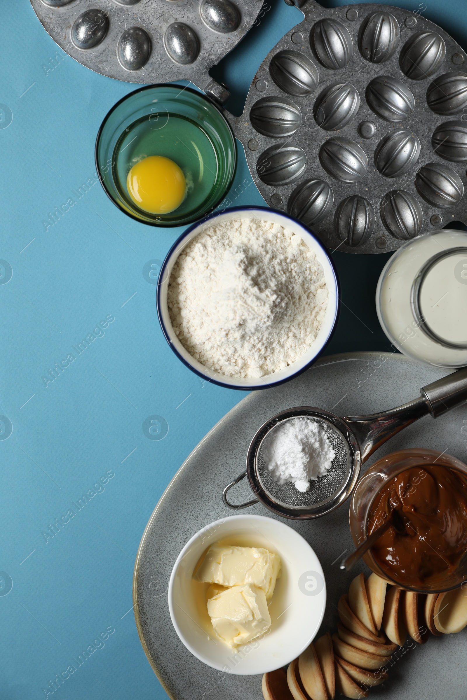 Photo of Baking dish and ingredients for walnut shaped cookies on light blue table, flat lay. Space for text