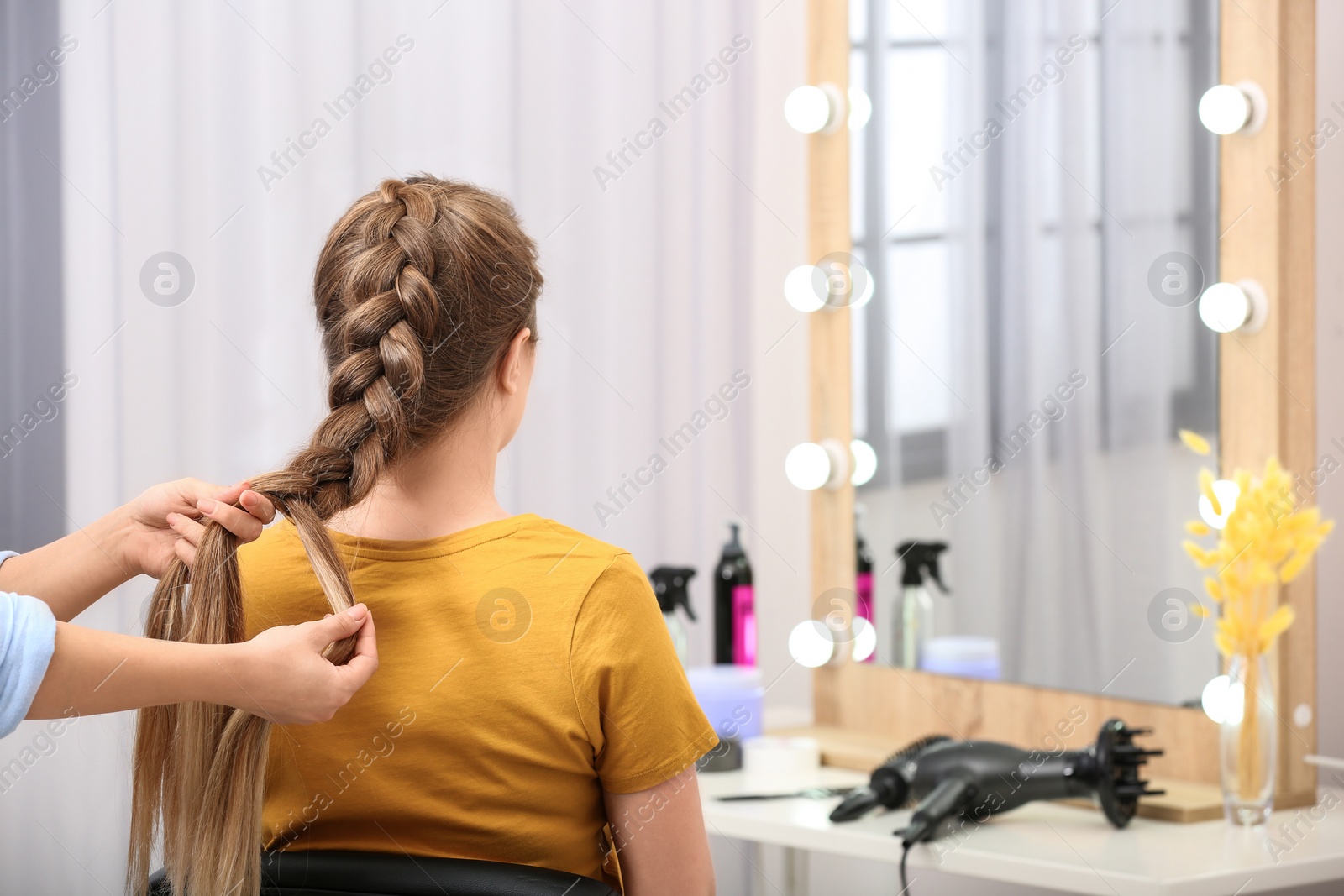 Photo of Professional coiffeuse braiding client's hair in salon