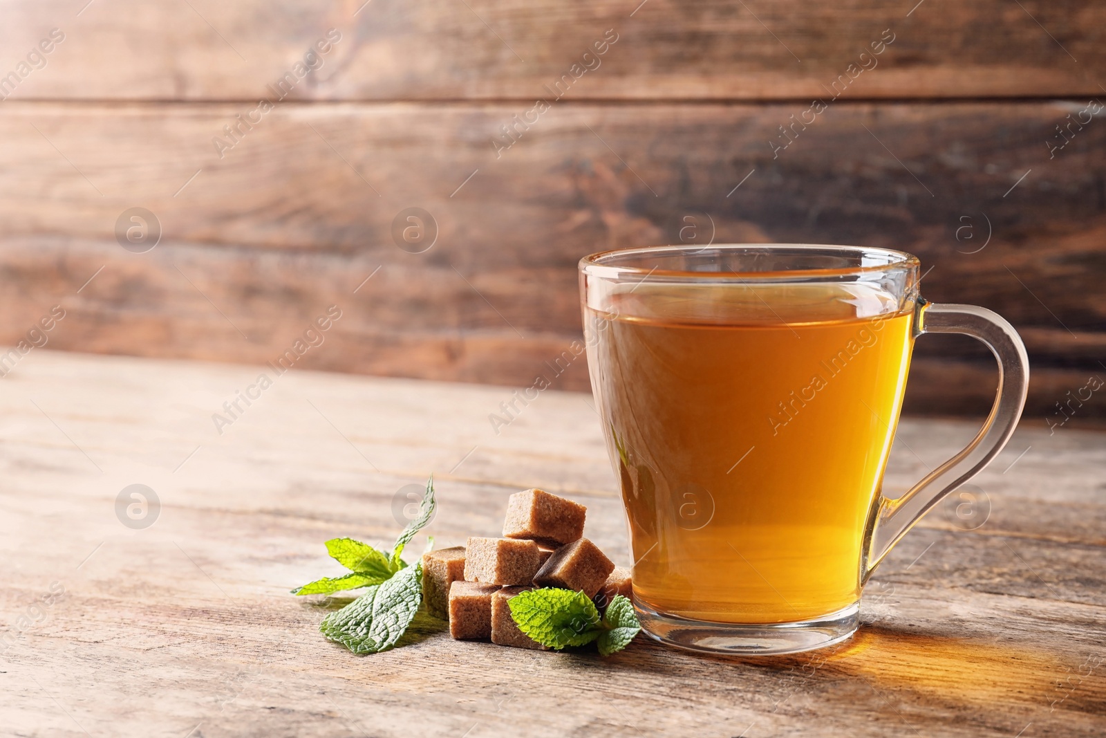 Photo of Cup with hot aromatic mint tea, fresh leaves and sugar cubes on wooden table