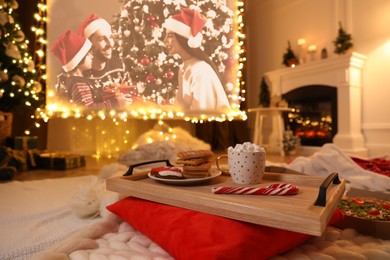 Image of Video projector screen displaying Christmas movie in room, focus on tray with snack and drink. Cozy winter holidays atmosphere