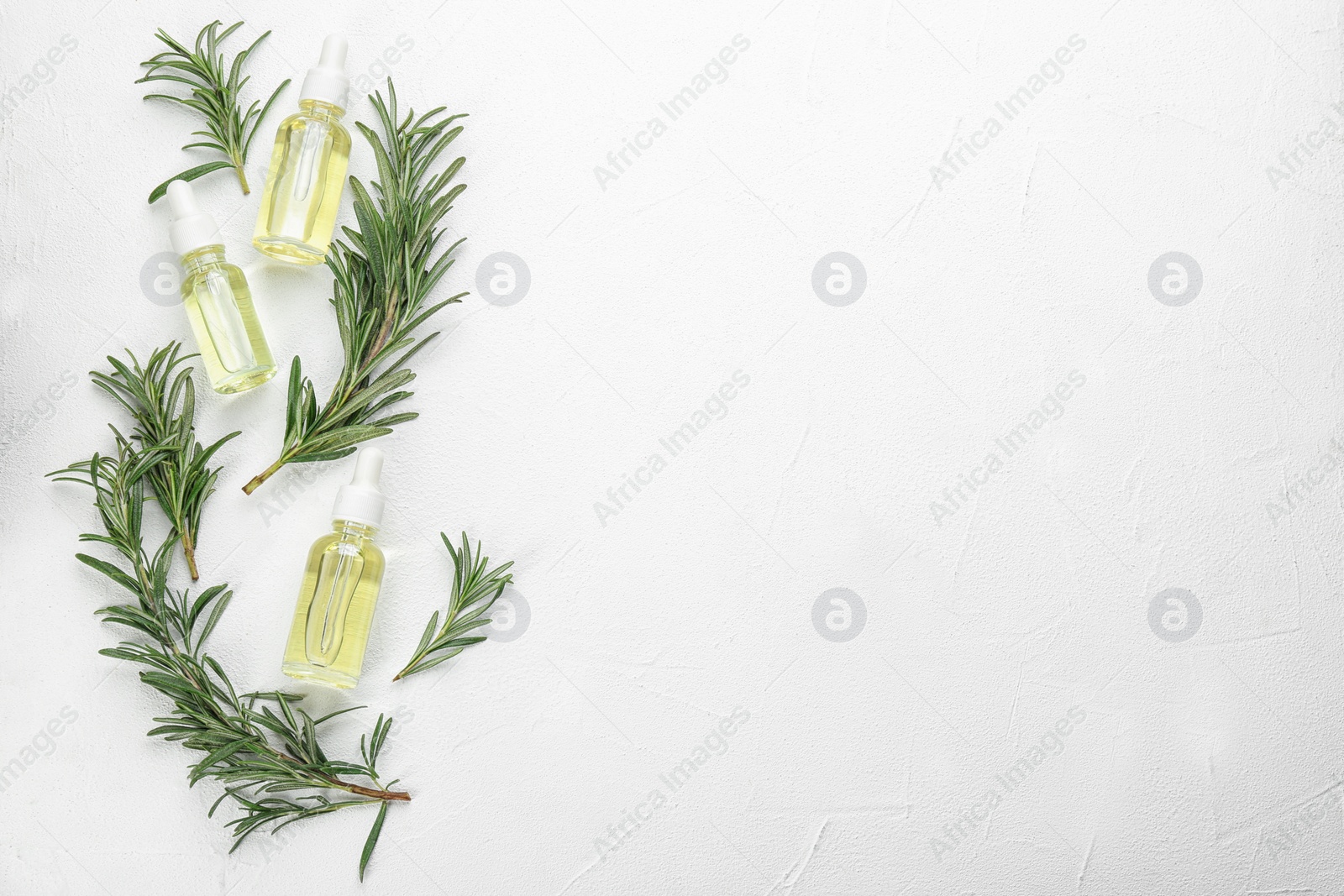 Photo of Fresh rosemary and bottles of essential oil on white table, flat lay. Space for text