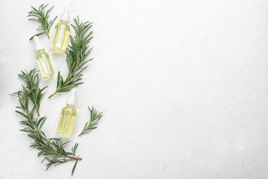 Photo of Fresh rosemary and bottles of essential oil on white table, flat lay. Space for text