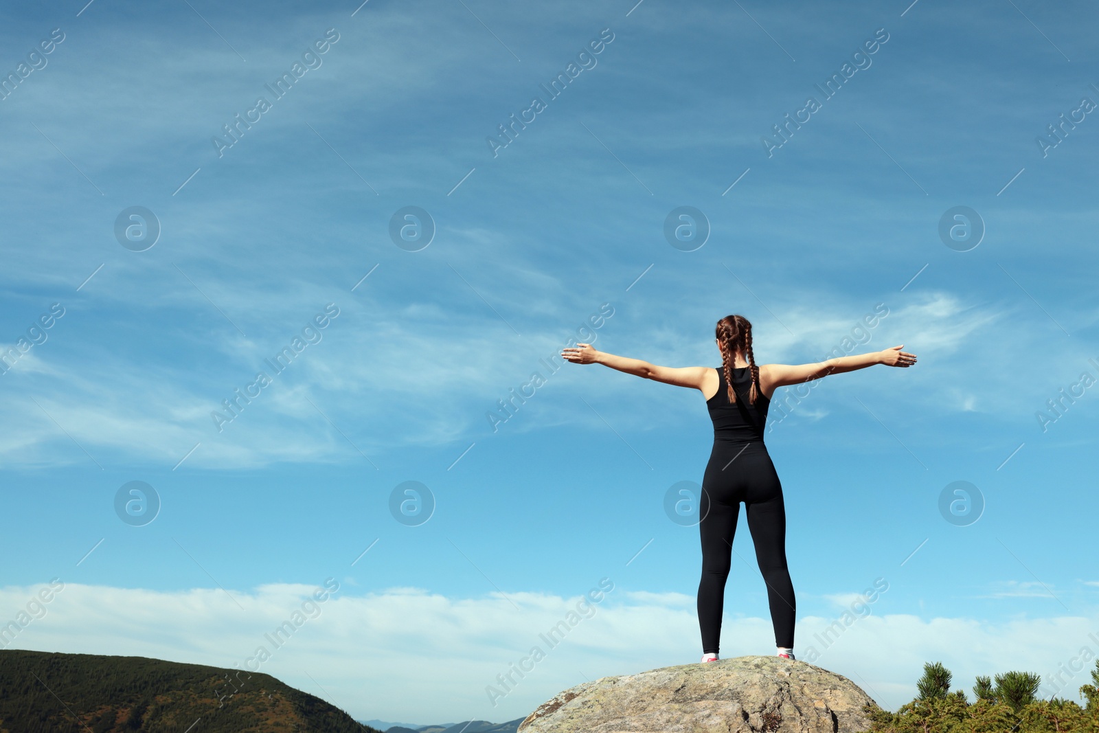 Photo of Beautiful young woman doing exercise on rock in mountains, back view