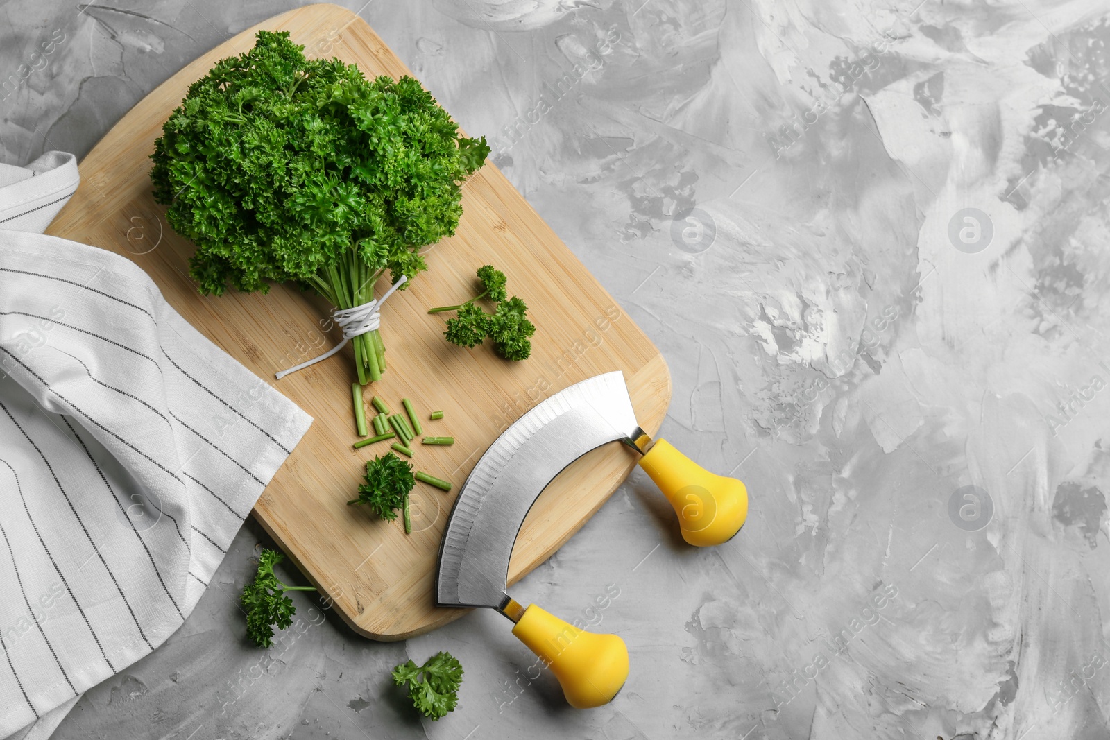 Photo of Fresh curly parsley, cutting board and mincing knife on grey table, flat lay. Space for text