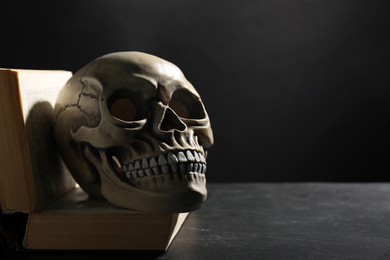 Human skull and old book on black table. Space for text