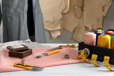 Photo of Set of sewing supplies and accessories with fabric on white wooden table indoors