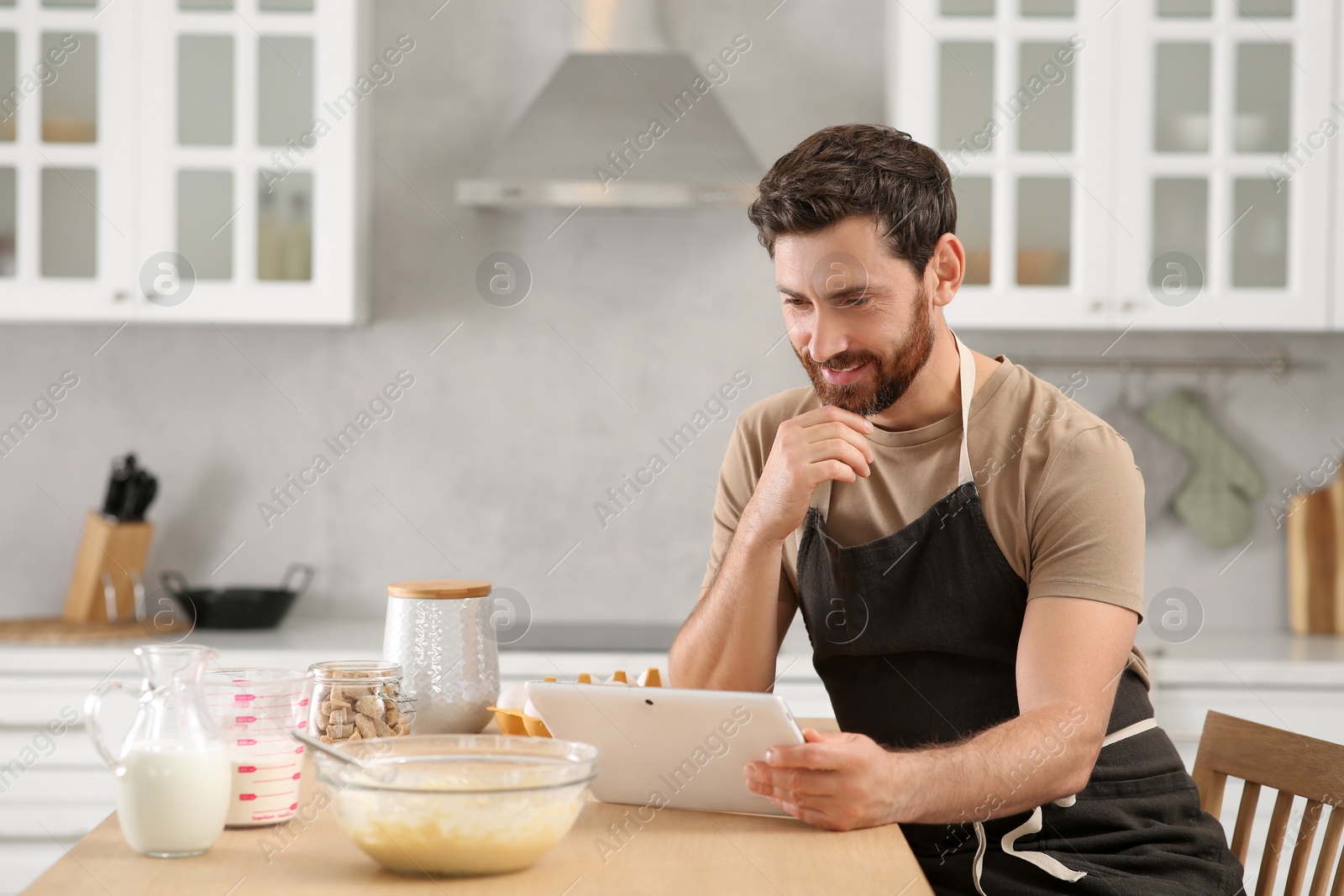 Photo of Man making dough while watching online cooking course via tablet in kitchen