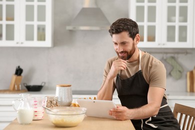 Man making dough while watching online cooking course via tablet in kitchen