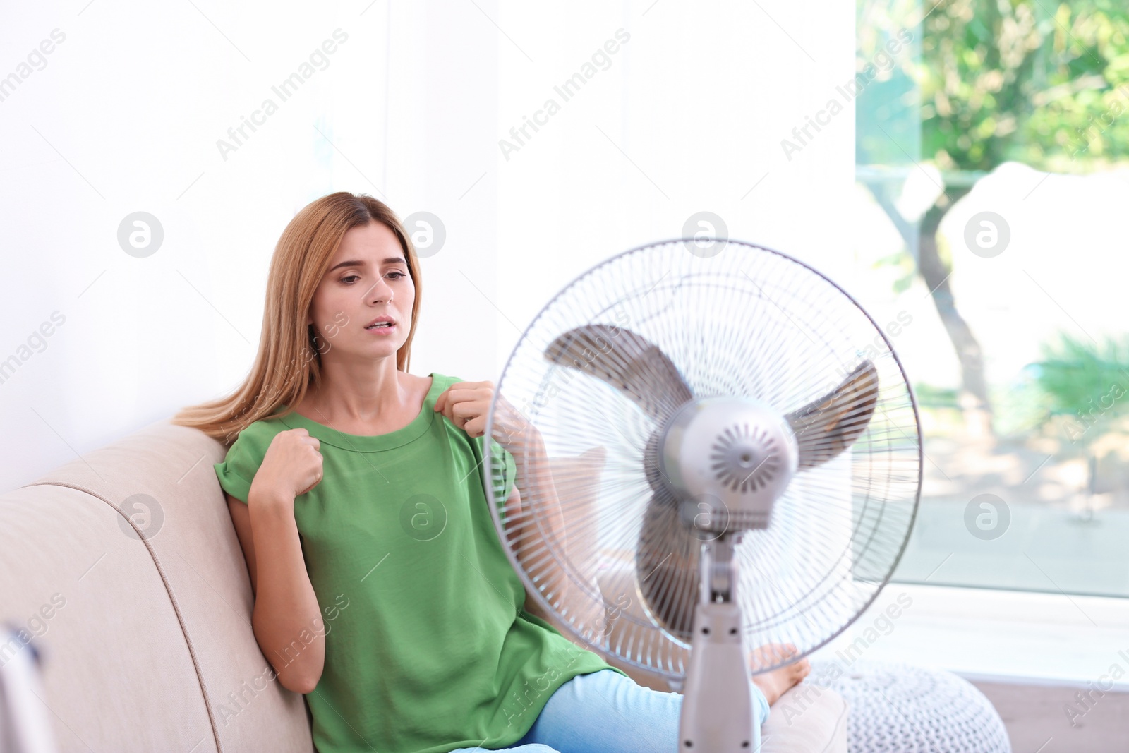 Photo of Woman suffering from heat in front of fan at home