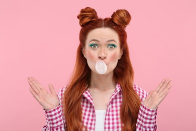 Photo of Portrait of surprised woman with bright makeup blowing bubble gum on pink background