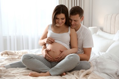 Photo of Young pregnant woman with her husband in bedroom