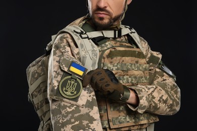 Photo of Soldier with Ukrainian flag and trident on military uniform against black background, closeup