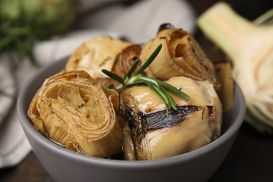 Photo of Bowl with delicious artichokes pickled in olive oil on table, closeup
