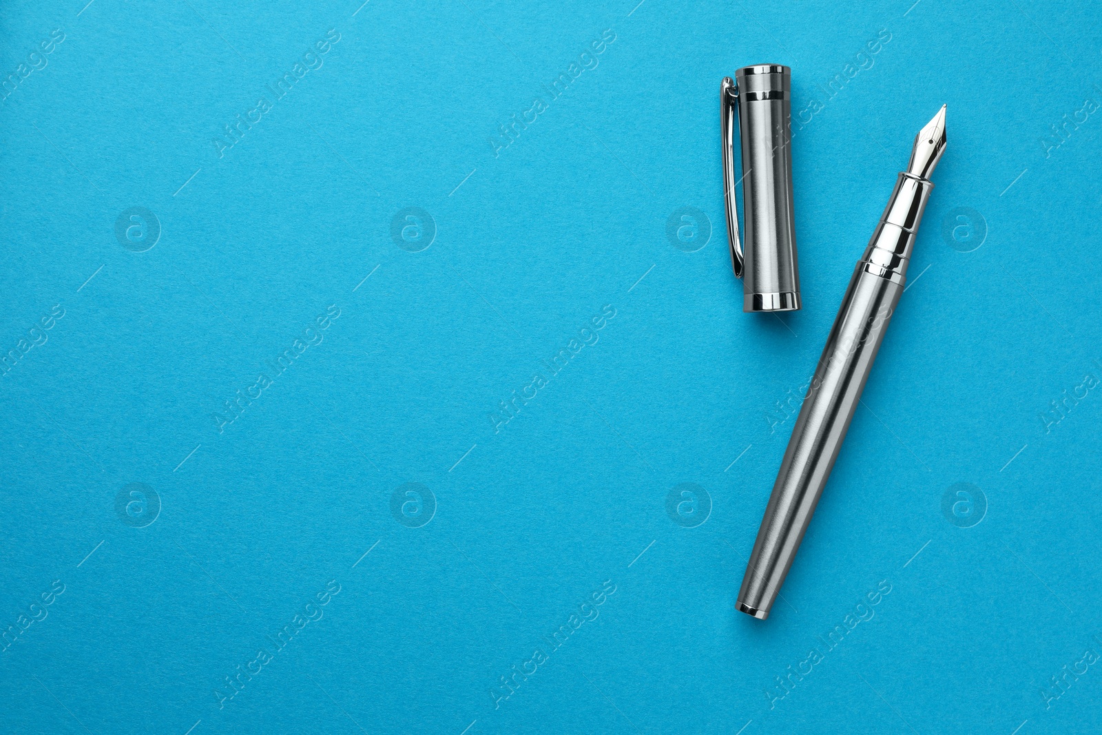 Photo of Stylish silver fountain pen with cap on light blue background, flat lay. Space for text