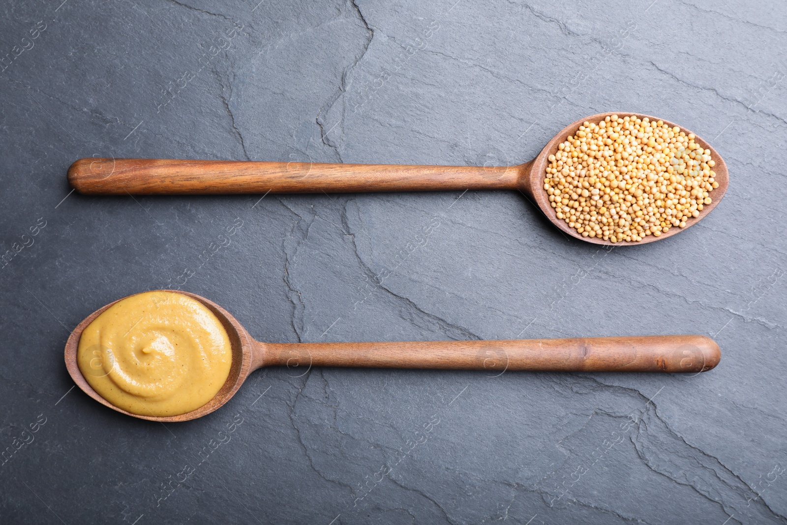 Photo of Mustard seeds and sauce in wooden spoons on grey table, flat lay