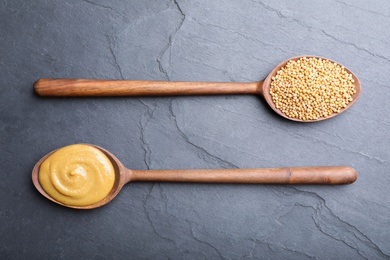 Mustard seeds and sauce in wooden spoons on grey table, flat lay