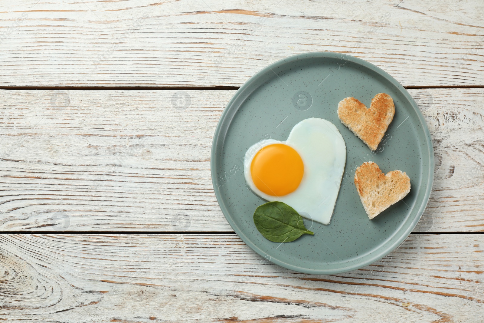 Photo of Romantic breakfast with heart shaped fried egg and toasts on white wooden table, top view. Space for text