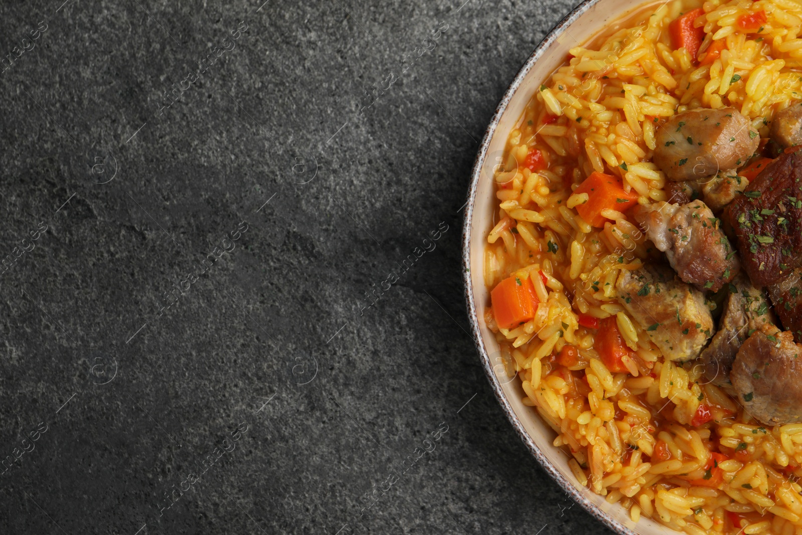 Photo of Delicious pilaf with meat on grey textured table, top view. Space for text
