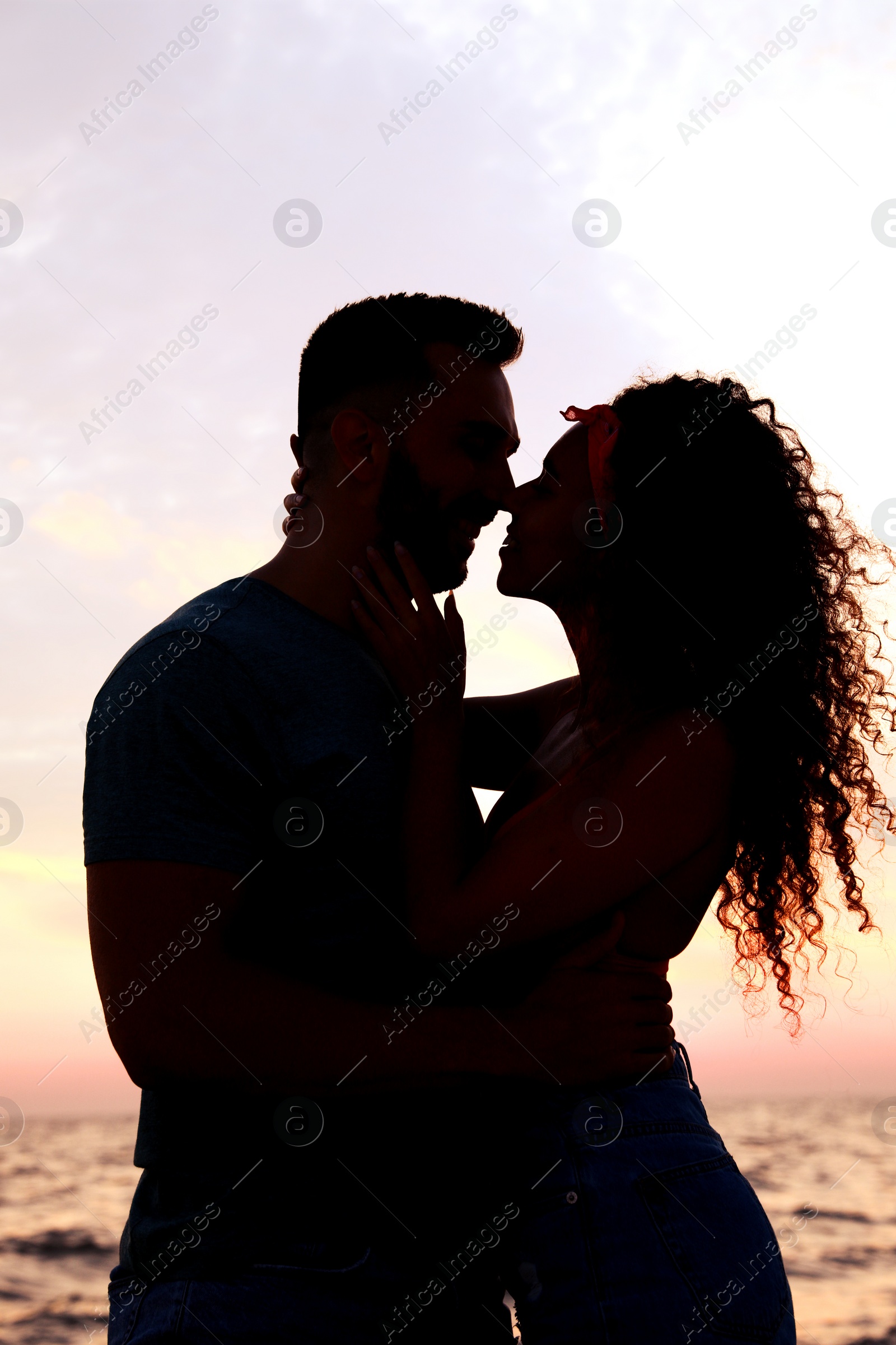 Image of Silhouette of lovely couple spending time together near sea at sunset