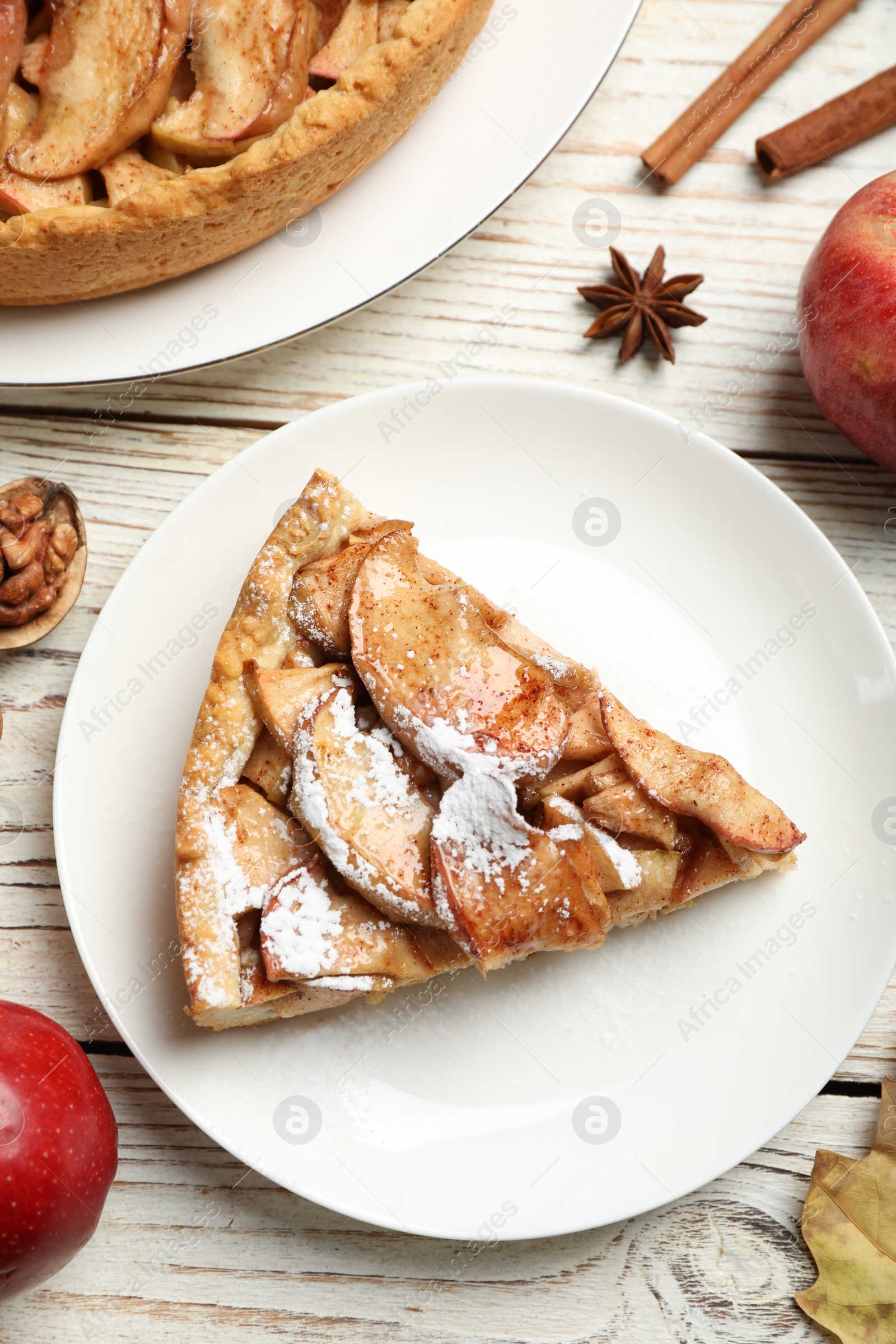 Photo of Slice of delicious apple pie with powdered sugar served on white wooden table, flat lay