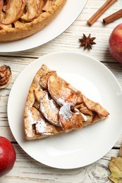 Slice of delicious apple pie with powdered sugar served on white wooden table, flat lay