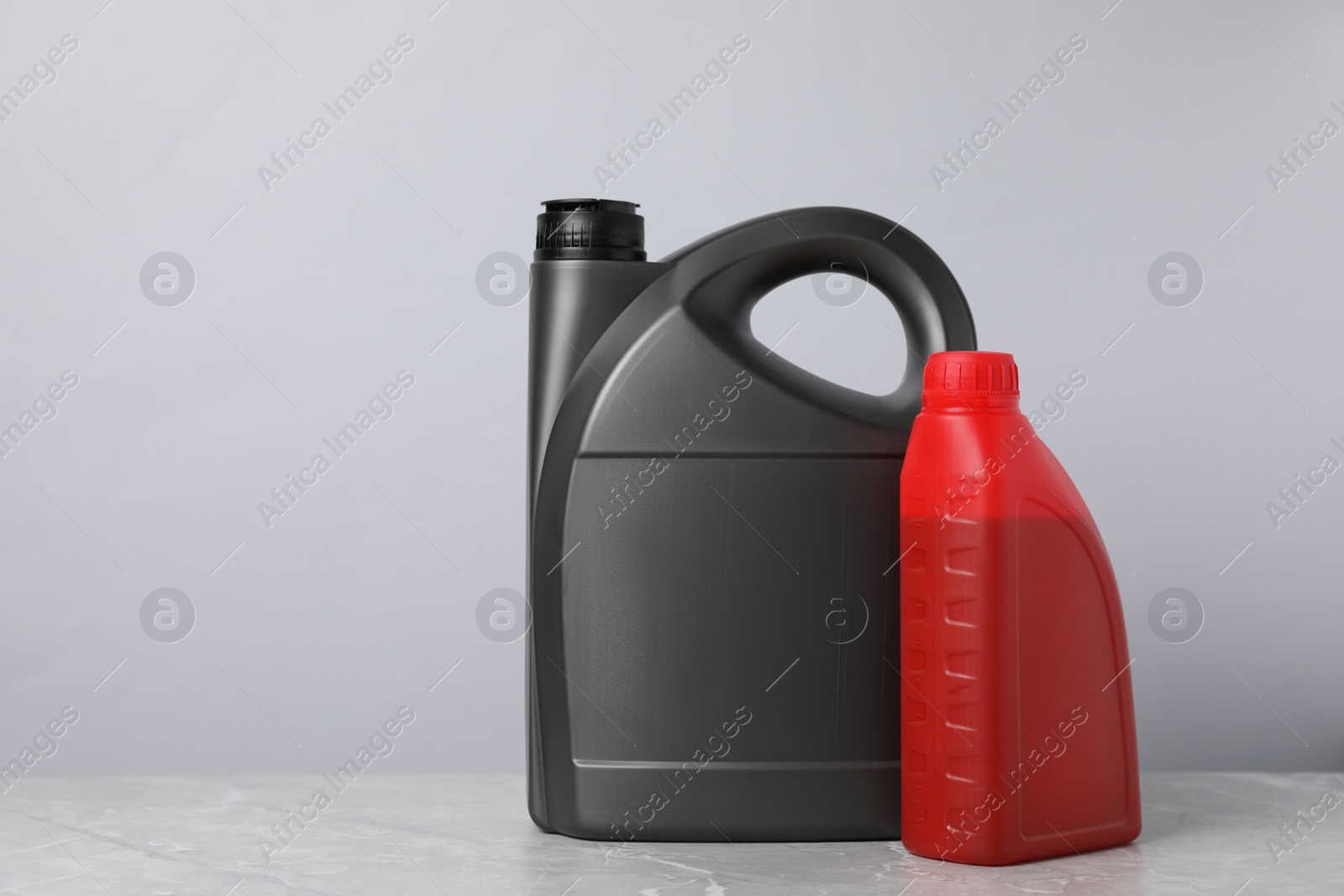 Photo of Motor oil in different canisters on grey marble table against light background, space for text