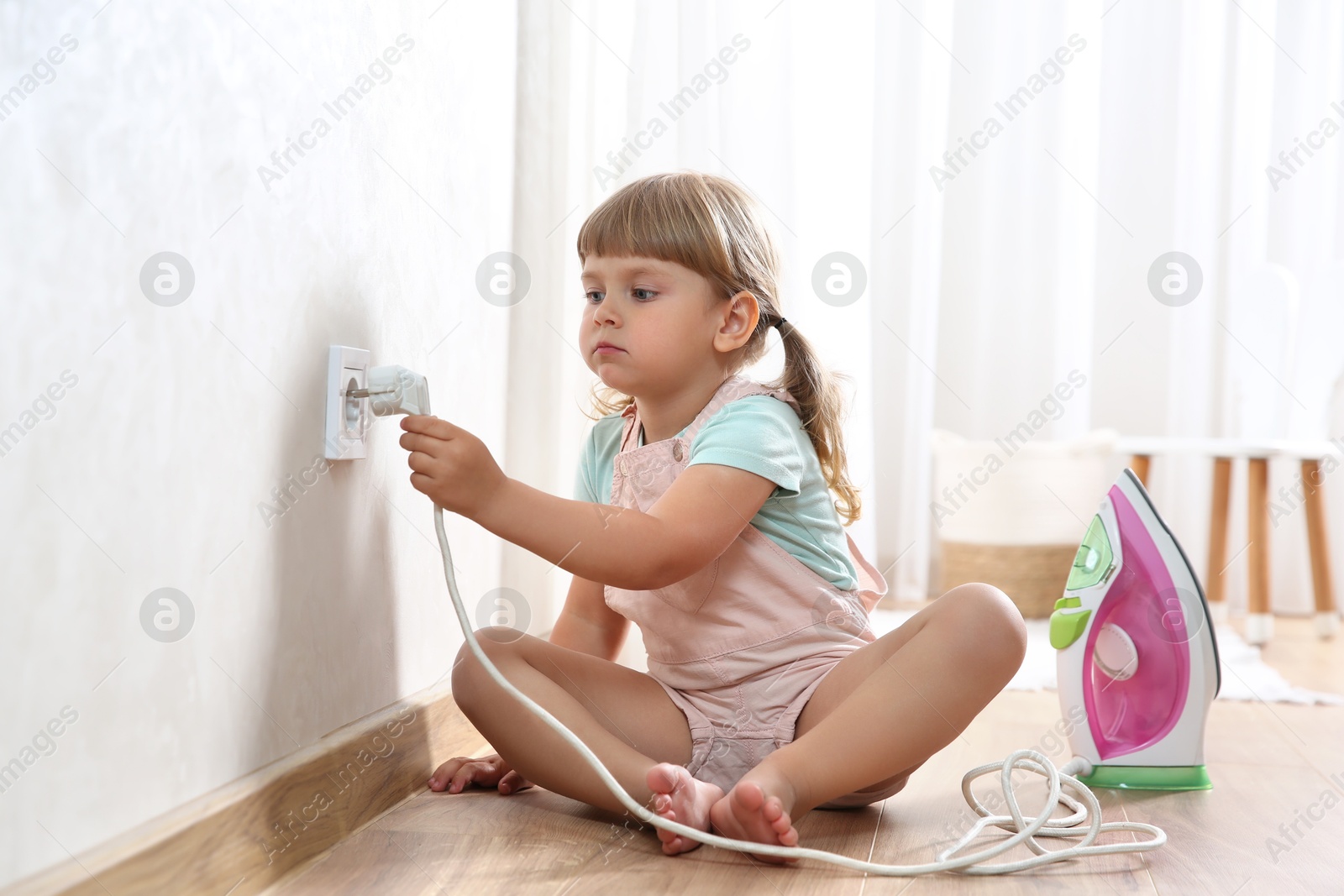 Photo of Little child playing with electrical socket and iron plug at home. Dangerous situation