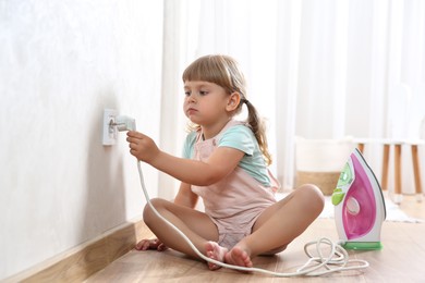 Photo of Little child playing with electrical socket and iron plug at home. Dangerous situation