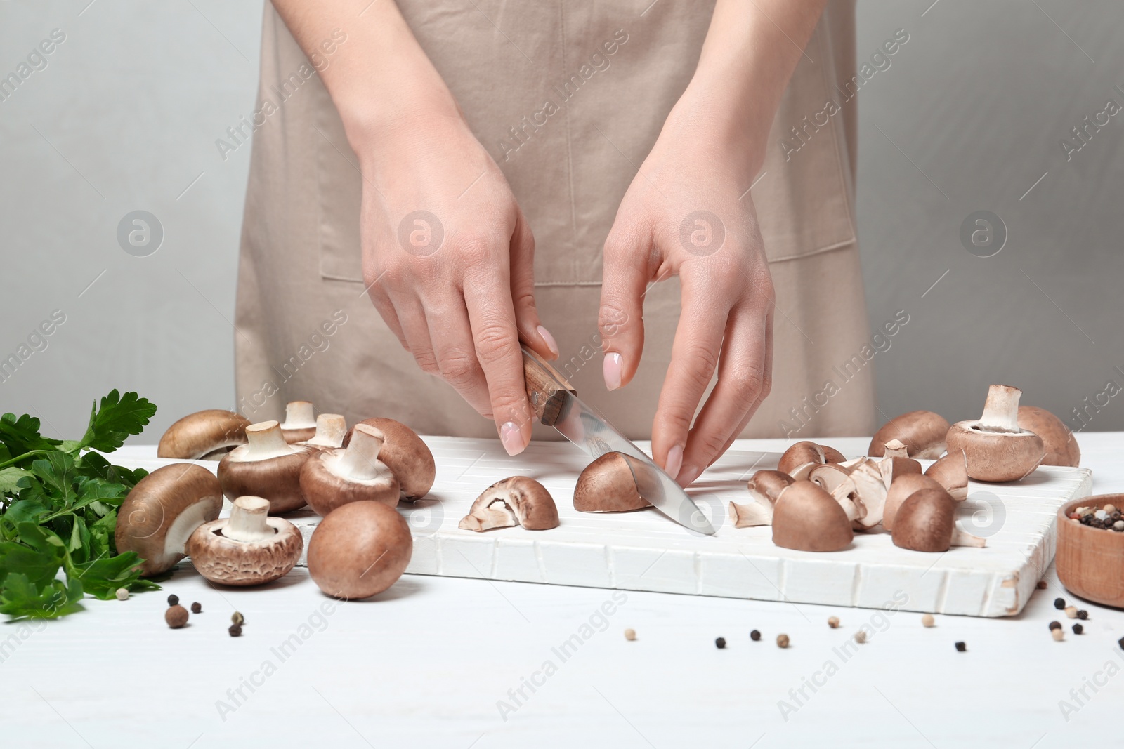 Photo of Young woman cutting fresh champignon mushrooms on wooden board, closeup view