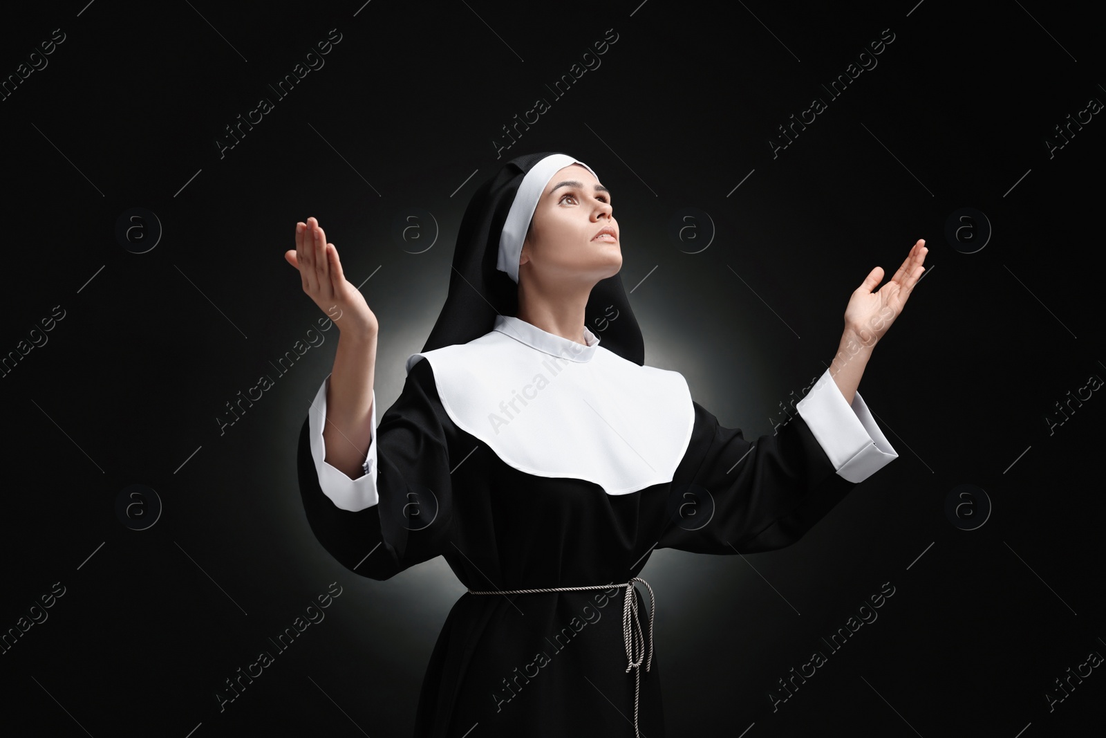 Photo of Nun praying to God on black background