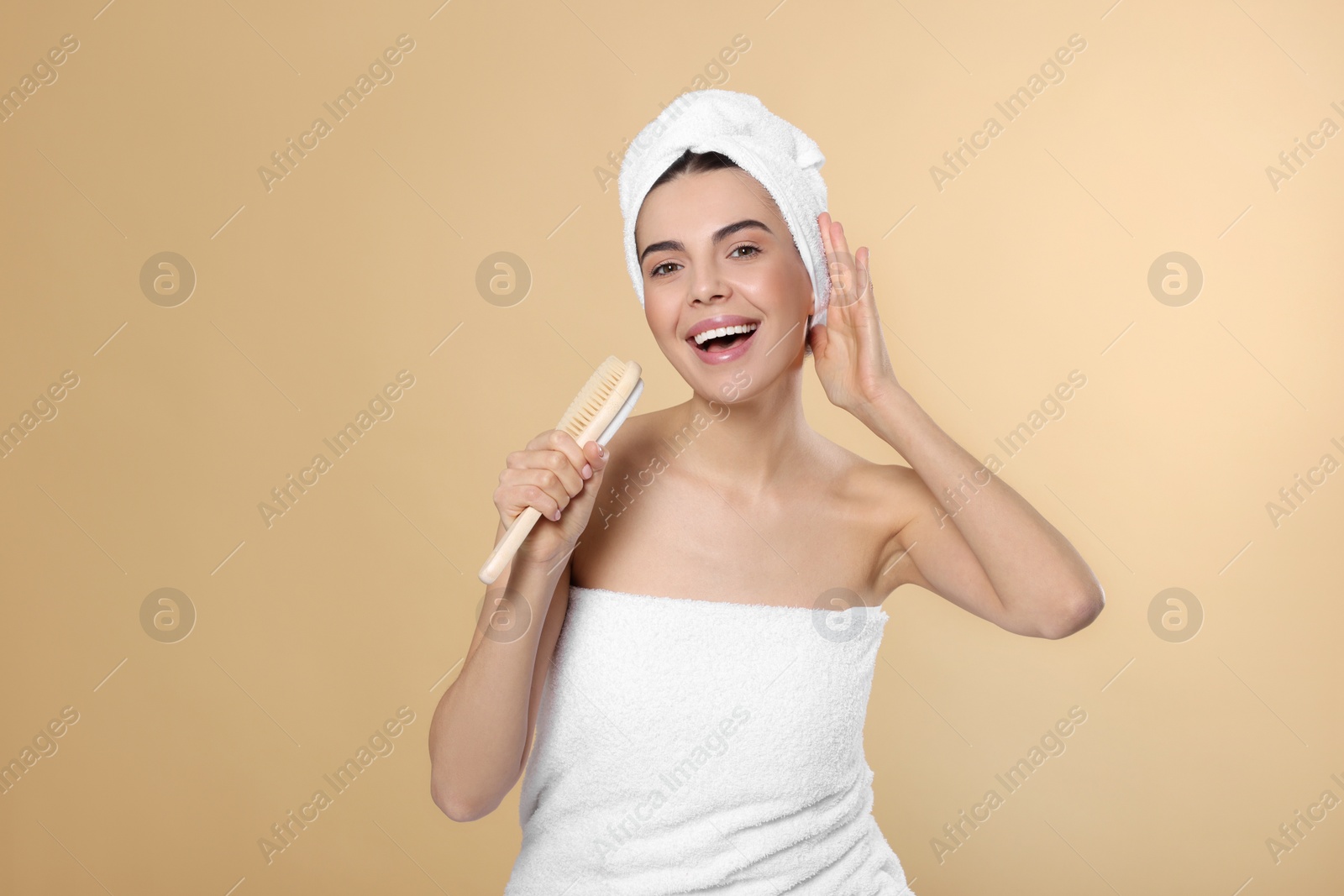 Photo of Happy young woman in towels singing into brush on beige background, space for text. Spa treatment