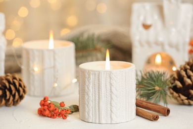 Holders with burning candles and decoration on white table against blurred Christmas lights