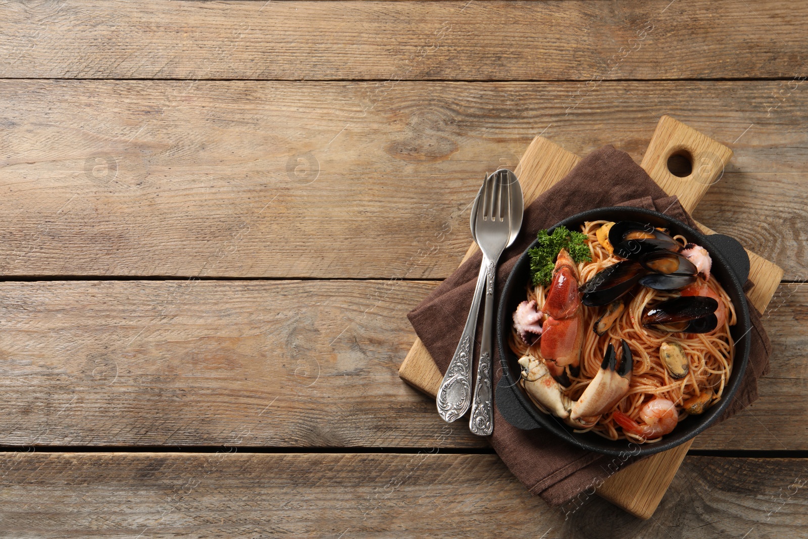 Photo of Delicious spaghetti with seafood served on wooden table, top view. Space for text