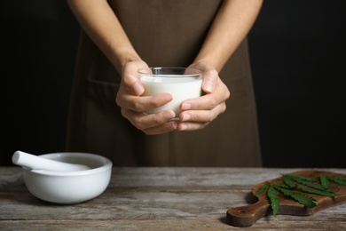 Photo of Woman holding glass of hemp milk near table, closeup