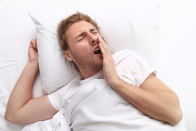 Photo of Handsome young man yawning while lying on pillow in morning, view from above. Bedtime