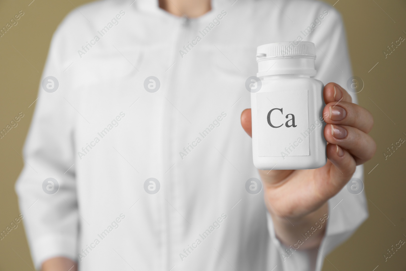 Photo of Calcium supplement. Doctor holding bottle with pills on beige background, closeup