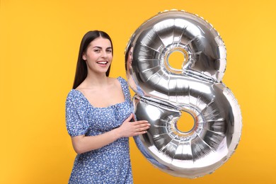 Happy Women's Day. Charming lady holding balloon in shape of number 8 on orange background