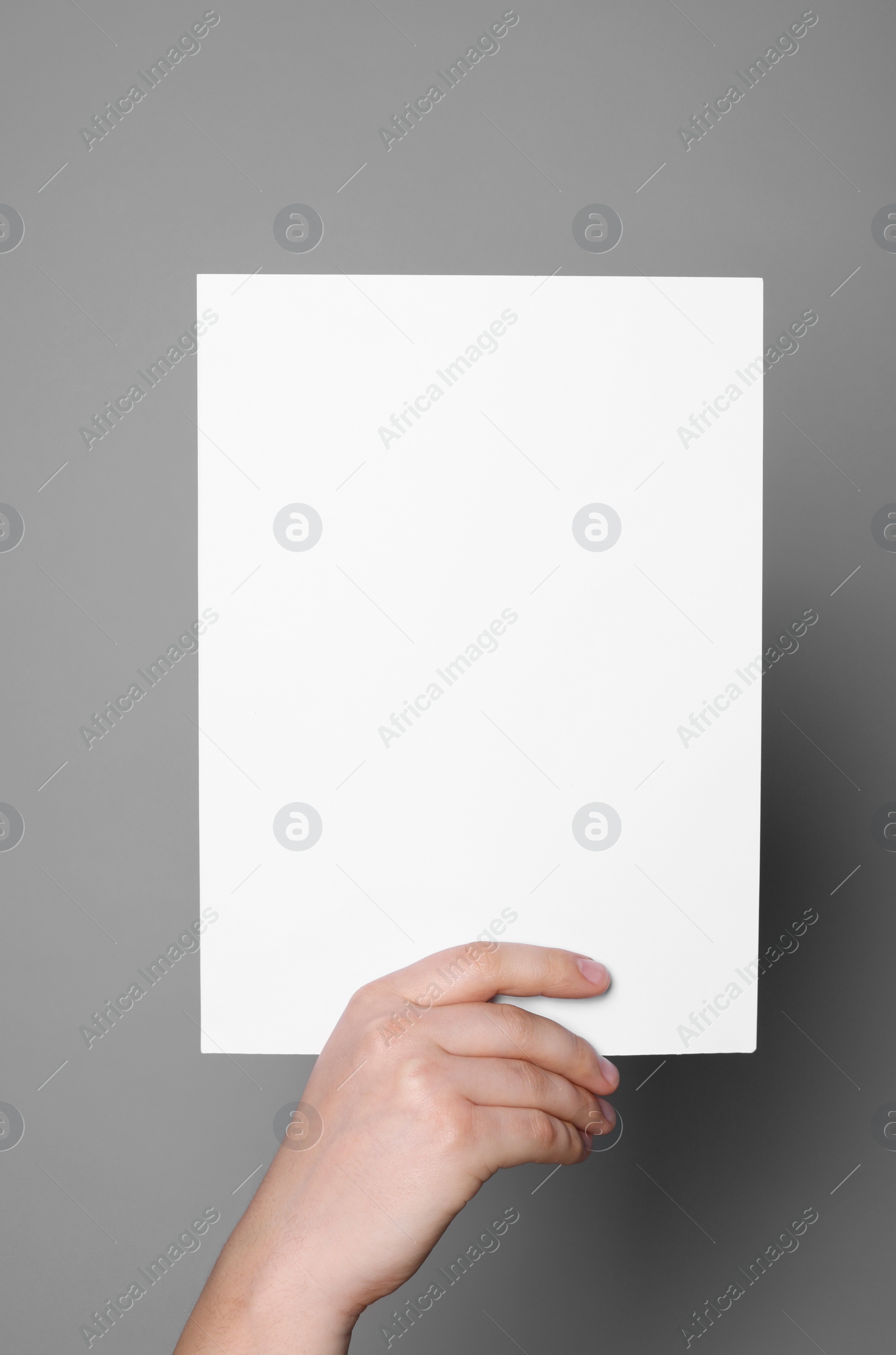 Photo of Woman holding sheet of paper on grey background, closeup. Mockup for design