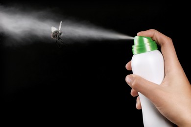 Woman spraying insect aerosol on fly against black background, closeup