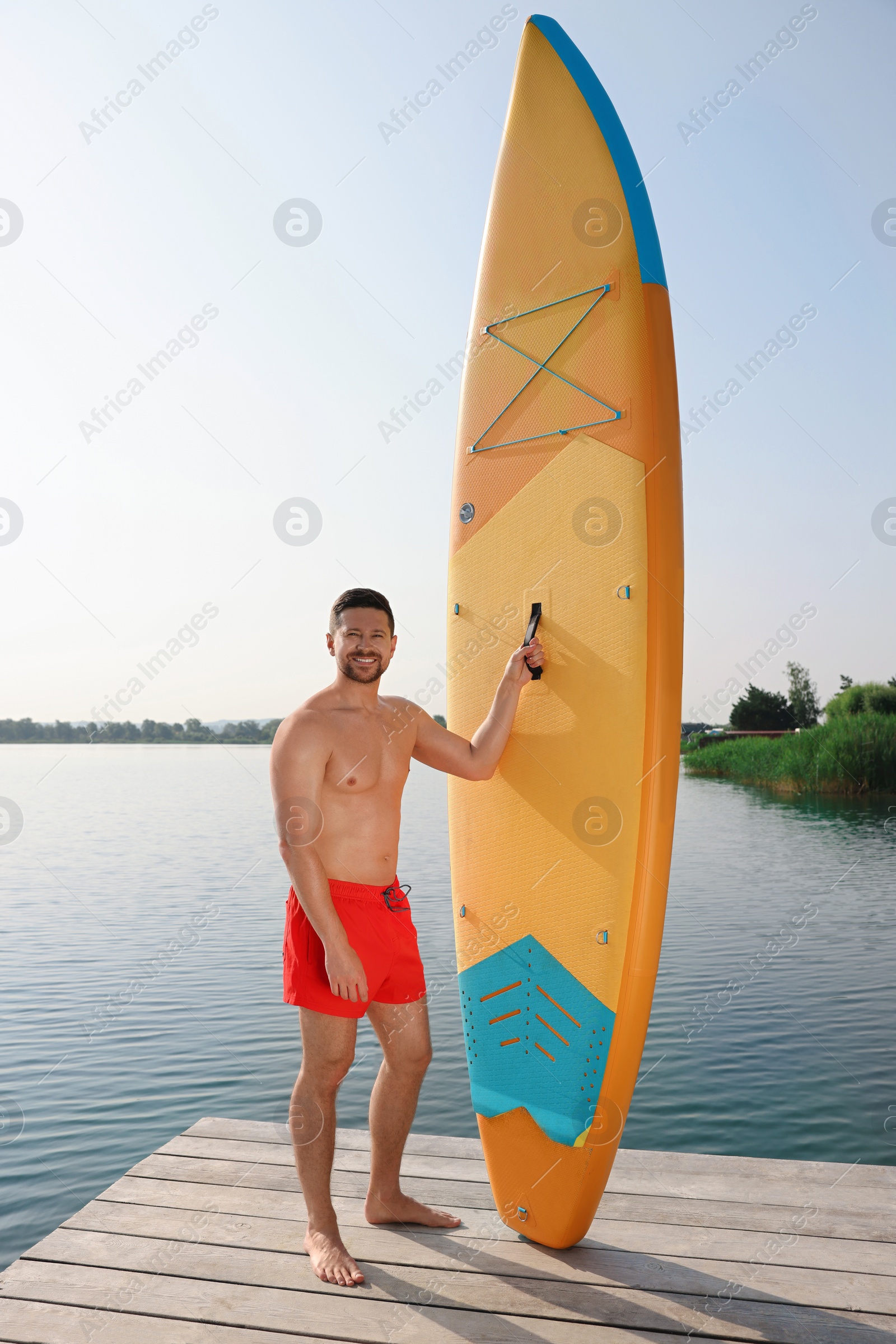 Photo of Man standing near SUP board on pier