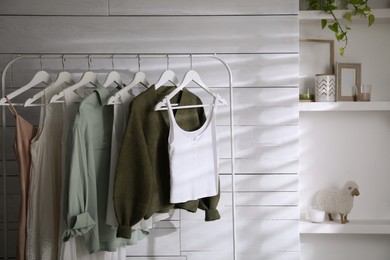 Photo of Rack with different stylish clothes near white wall in dressing room. Interior design