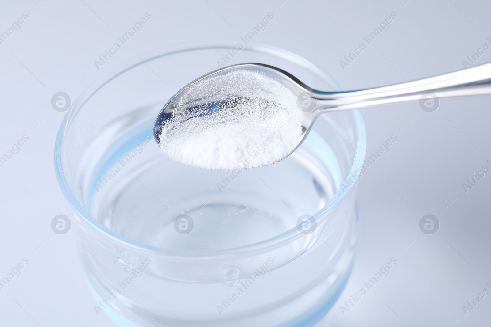 Photo of Adding baking soda into glass of water on light background, closeup