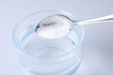 Photo of Adding baking soda into glass of water on light background, closeup